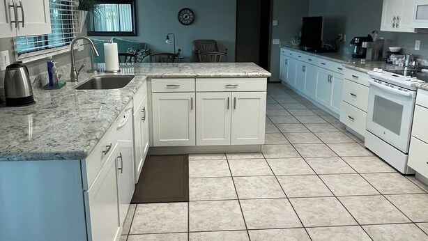 Uma cozinha moderna com armários brancos, uma ilha grande e piso revestido de azulejos.