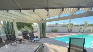 Um pátio externo com piscina, cadeiras e mesa.