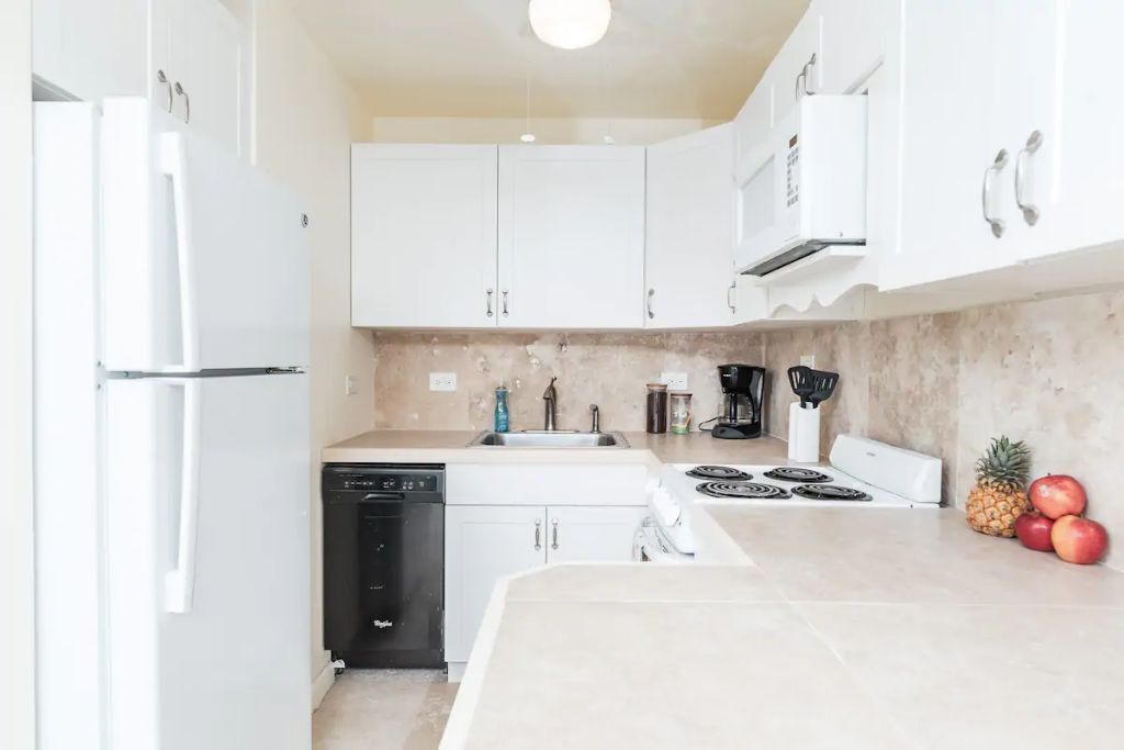 A modern kitchen with white cabinets, a dishwasher, a stove, and a sink.
