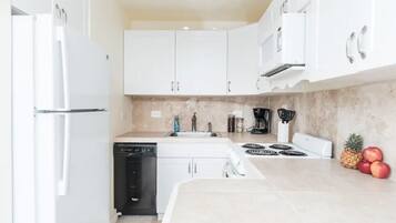 A modern kitchen with white cabinets, a dishwasher, a stove, and a sink.