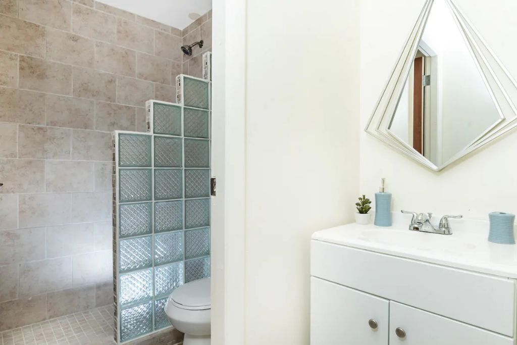 Ein Badezimmer mit Duschkabine aus Glas, einer weißen Toilette und einem Waschbecken mit Spiegel darüber.