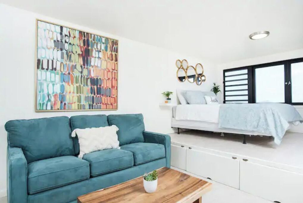 A modern living room with a teal sofa, a coffee table, and a colorful abstract painting on the wall.
