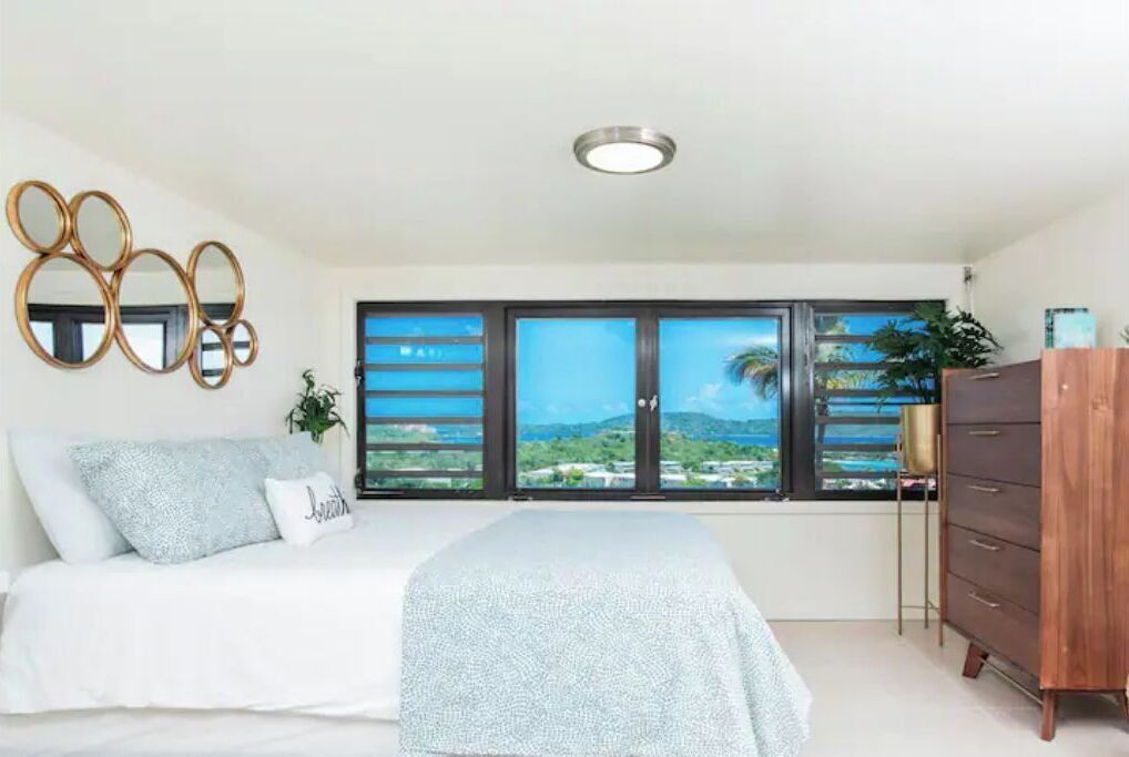 A bedroom with a bed, a dresser, a window with a view, and a ceiling light.