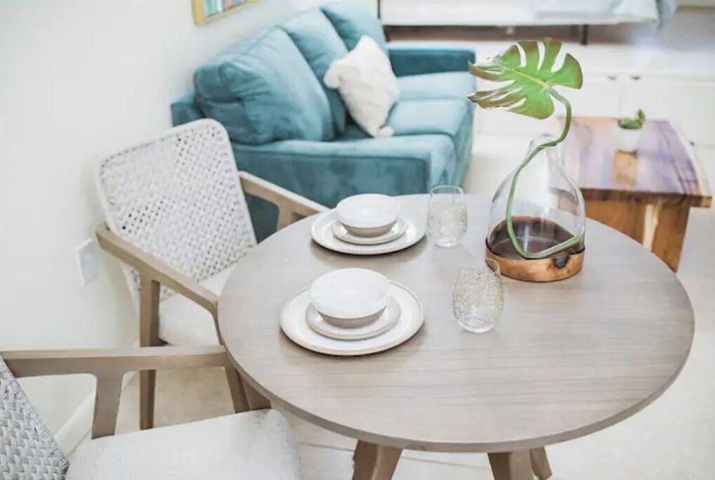Una mesa redonda de madera con platos blancos, un vaso transparente y una olla de cobre.