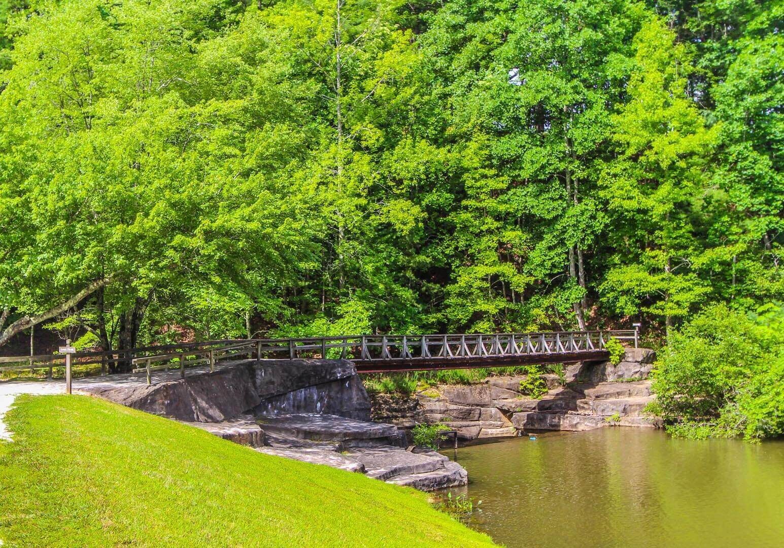 Un pont de pierre enjambe un étang, entouré d’arbres verdoyants.