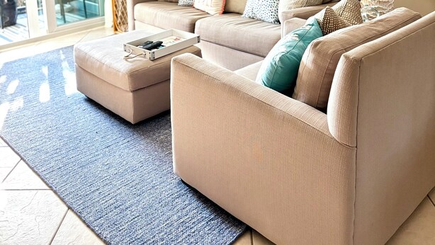 En stue med en beige sofa, et sofabord og to lamper. Der er et maleri på væggen og en dør, der fører ud til en balkon.