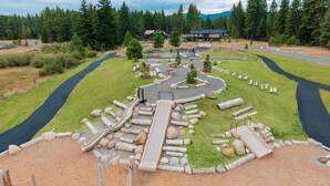 Un terrain de jeux avec des toboggans et des structures d’escalade, entouré d’un espace paysager agrémenté d’arbres et avec une route en arrière-plan.