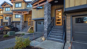 Un immeuble résidentiel moderne à plusieurs étages, doté d’une façade en bois, de piliers en pierre et d’une voiture garée dans l’allée.