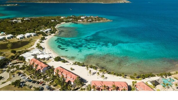 An aerial view of a coastal resort with a beachfront, clear waters, and distant islands. - Charming Beach Condo w/ Balcony (Smith Bay)