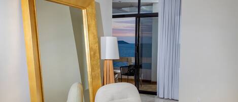 Une chambre moderne avec un grand miroir à cadre doré, un fauteuil blanc et une petite table en laiton posée sur un tapis tissé.