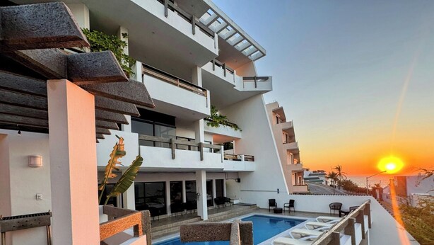 Un edificio moderno de varios pisos con piscina en la azotea y zona de estar al aire libre.