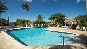 A clear blue swimming pool surrounded by lounge chairs and palm trees.