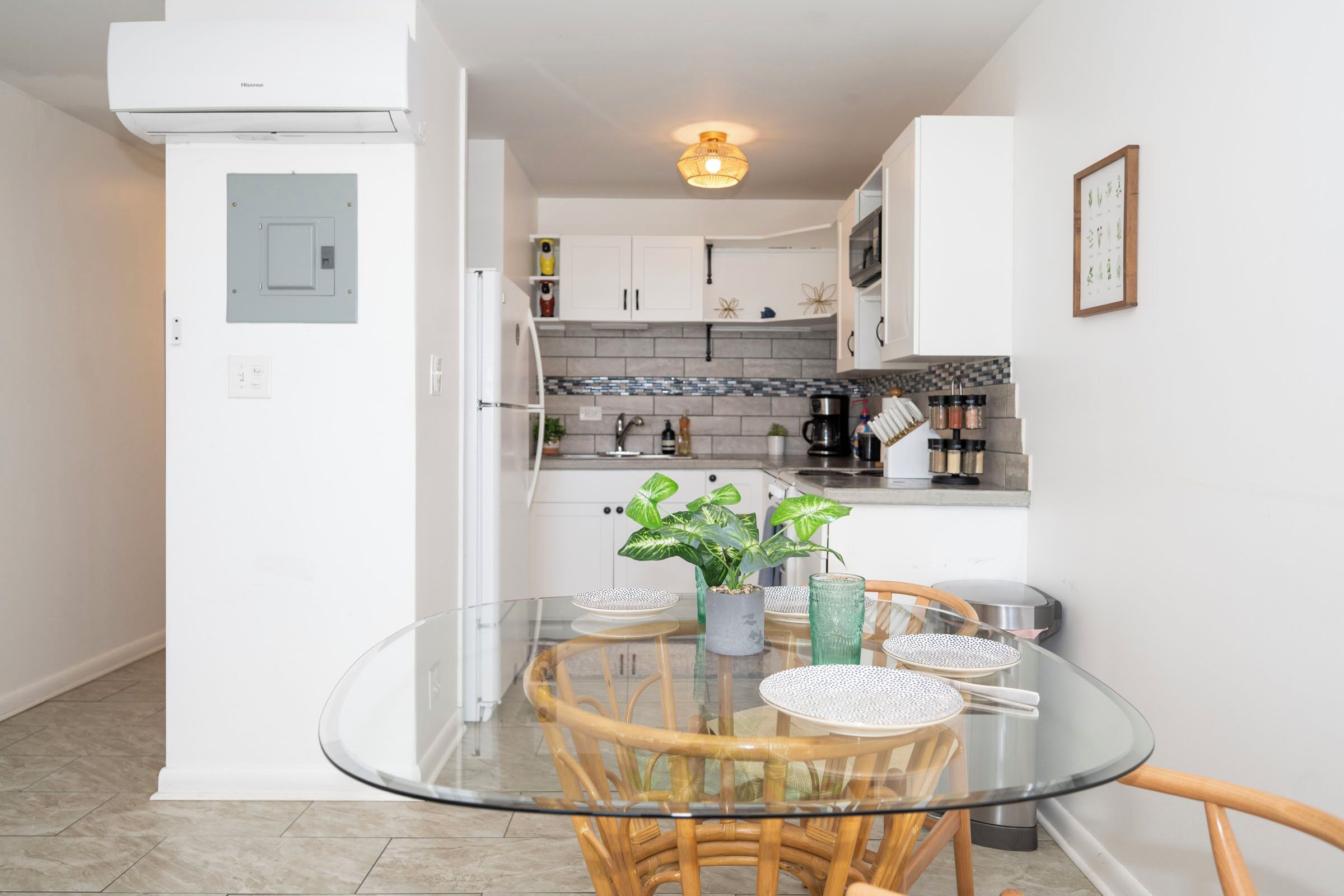 A compact kitchen with white cabinets, a glass dining table, and a potted plant.