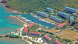 Eine Luftaufnahme eines Küstenhotels mit mehreren Gebäuden, einer Marina mit Booten und einem Strand.