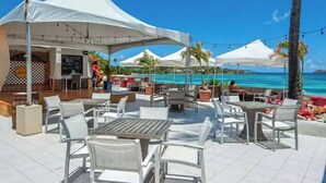 Eine Außenpatio mit weißen Tischen und Stühlen, einem weißen Zelt und Blick auf das Meer.