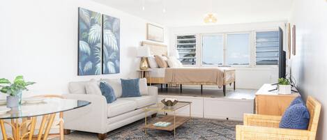 A living room with a sofa, coffee table, and chairs, a dining table with chairs, a ceiling fan, and a large window with a view.