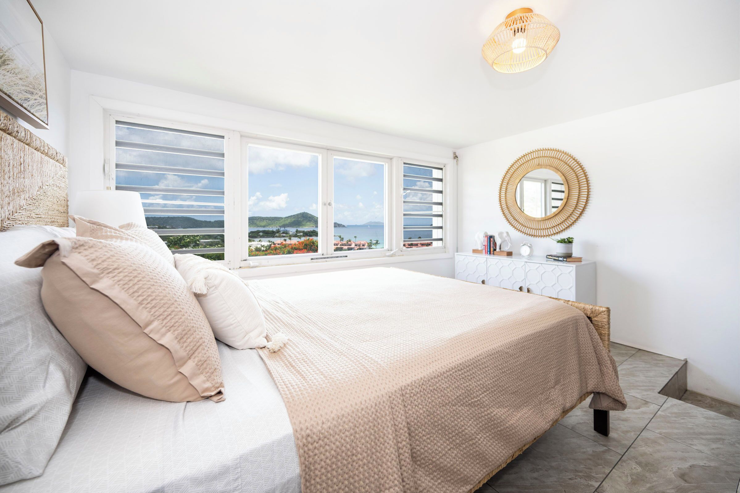 Une chambre avec un grand lit, une table de chevet, un miroir et une vue sur la mer.