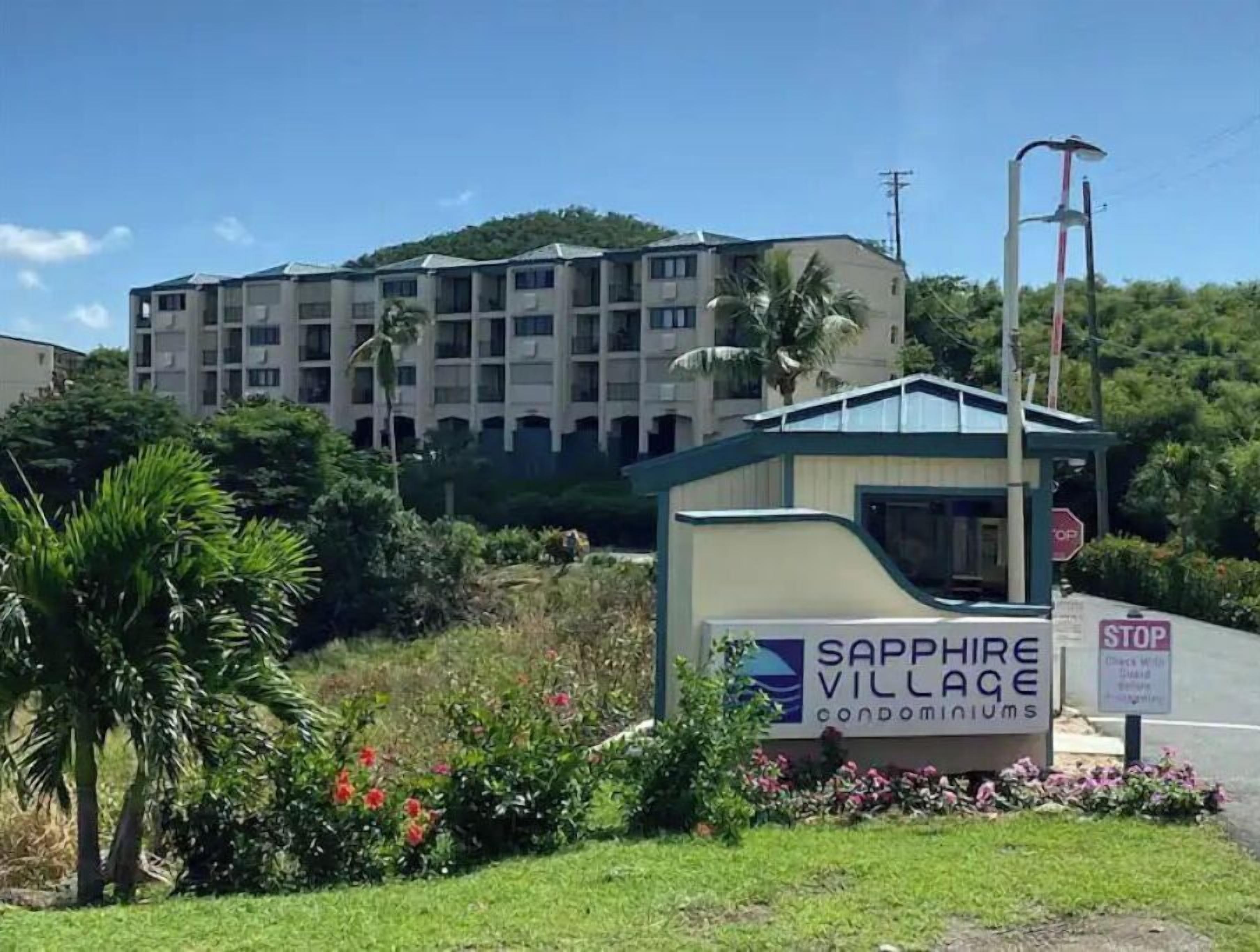 A sign for Sapphire Village condominiums with a view of a multi-story building in the background.