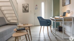 Un soggiorno moderno con un divano grigio, una scacchiera, una poltrona blu e una scrivania con un portatile.