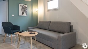 Un soggiorno con un divano grigio, un tavolino rotondo in legno, una poltrona nera, una scacchiera e un quadro con uno zebro.