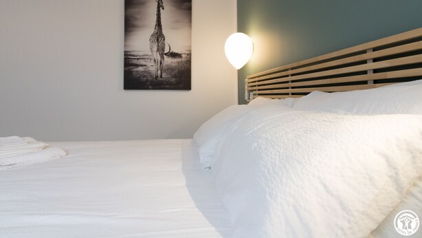 Una camera da letto con un letto, un quadro appeso raffigurante una giraffa, una luce a parete rotonda e una testiera in legno.