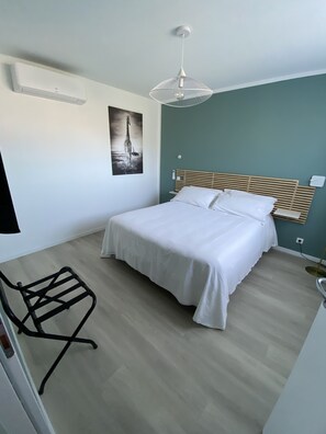 Een slaapkamer met een bed, een stoel, een wandairconditioner, een plafondlamp en een poster met een giraffe.