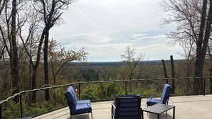 Un área de estar al aire libre con sillas y una mesa, con vista a un paisaje boscoso.