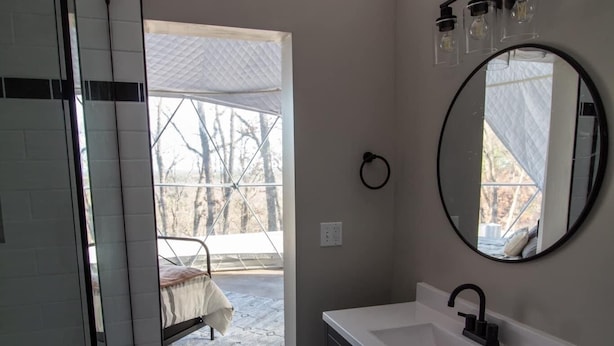 Un baño con lavamanos blanco, muebles oscuros, espejo redondo y tragaluz.