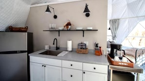 Cocina compacta con refrigerador, lavamanos y encimera con una cesta y utensilios.