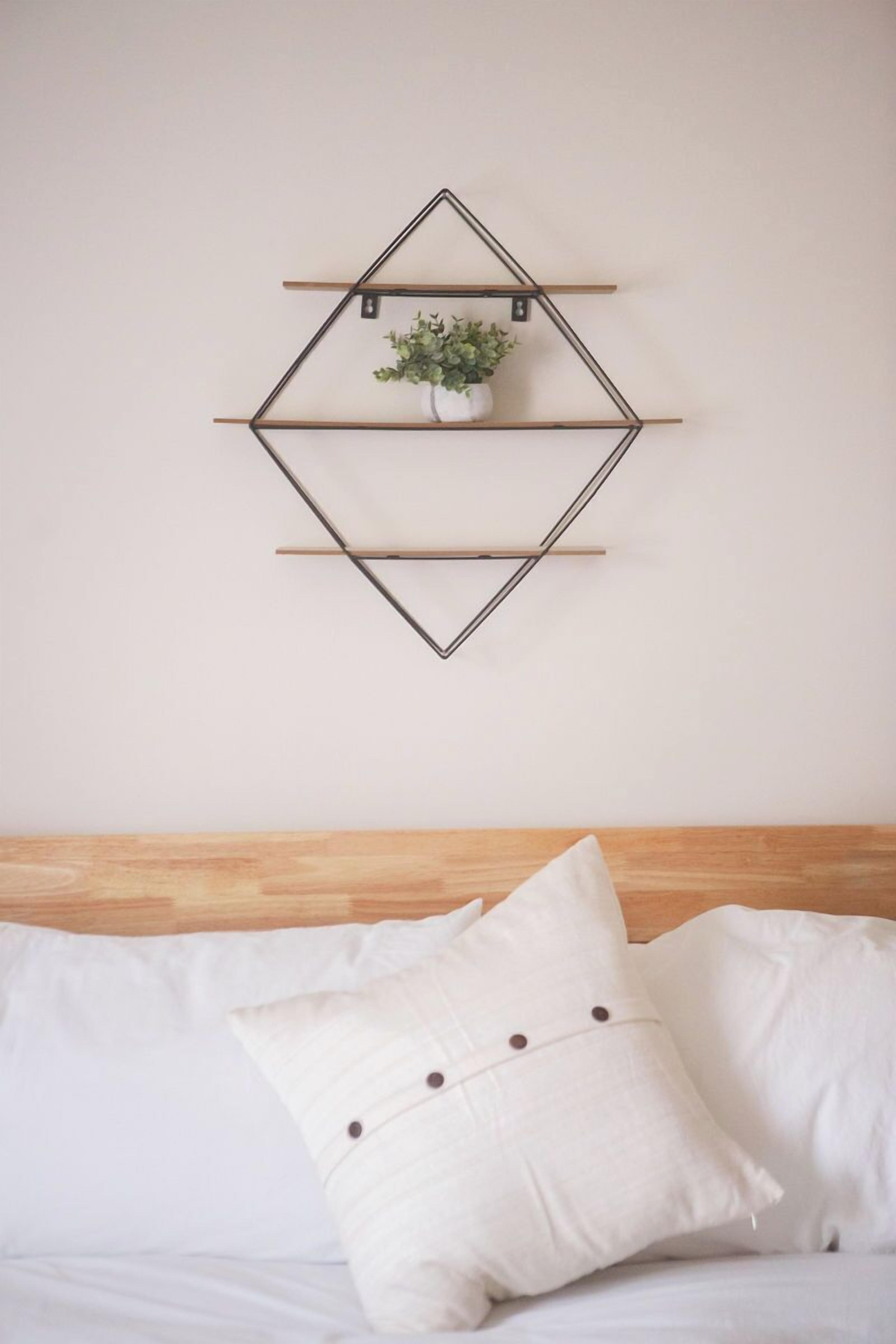 Een bed met witte beddengoed en één kussen, een houten hoofdbord en een wandplank met een plant.