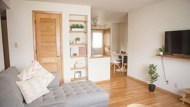 Een moderne woonkamer met een grijze bank, houten planken, een eethoek en een televisie.