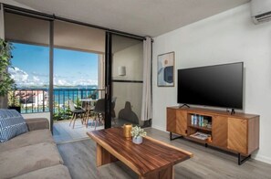 Relax in this stylish living room with a large flat-screen TV, comfortable sofa, and sliding glass door leading to a balcony with a sea view.