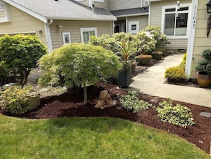 A residential house with a well-maintained garden, including various shrubs and a decorative sculpture. - Beautiful, secure, private townhouse in Silverdale. (Silverdale)