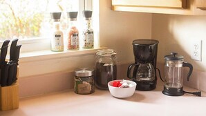 A kitchen with wooden cabinets, a window with blinds, a coffee maker, a blender, and various kitchen utensils and containers. - Cozy Modern Garden Flat (Westerville)