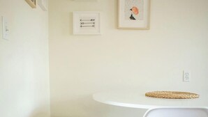 A minimalist room with a white table and chair, a small white bench, and three framed artworks on the wall. - Cozy Modern Garden Flat (Westerville)