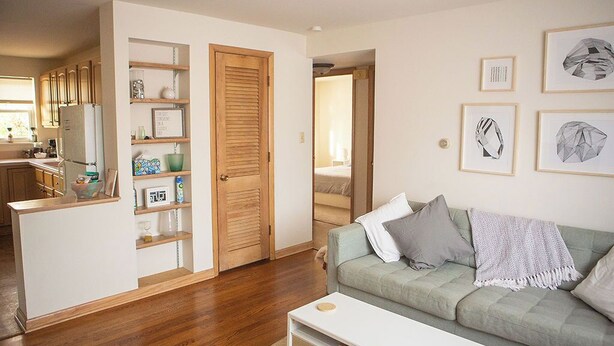 A living room with a green sofa, a white coffee table, and a kitchen area with wooden cabinets and a refrigerator. - Cozy Modern Garden Flat (Westerville)