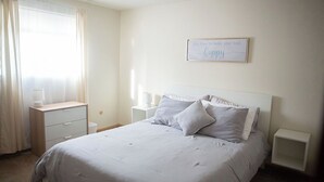 A neatly arranged bedroom with a bed, bedside tables, a nightstand, a lamp, and a window with curtains. - Cozy Modern Garden Flat (Westerville)