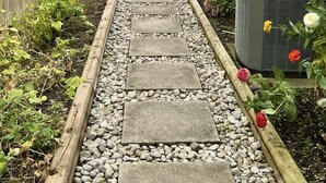 Un vialetto tra il giardino conduce a un portico di legno, con un prato e una casa sullo sfondo.
