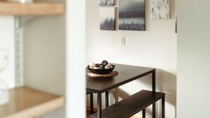 A modern dining area with a wooden table and bench, a potted plant, and three framed artworks on the wall.