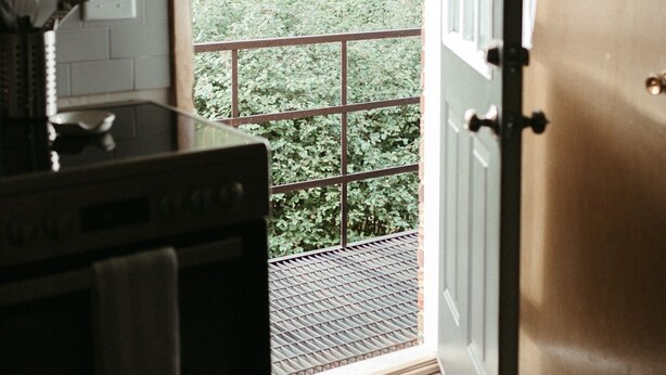 A kitchen with a stove, a window, and a door leading to a balcony with a view of greenery.