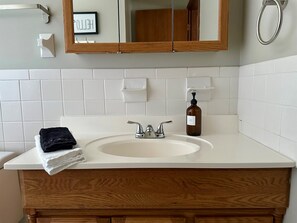 Ein Badezimmer mit einem weißen Waschbecken, einem Holzkosmetikschrank, einem Spiegel, einem Handtuch und einer Seifenspender.