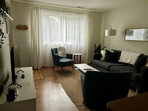 Ein Wohnzimmer mit Sofa, Sesseln, Couchtisch und Fernseher auf einem Schrank.