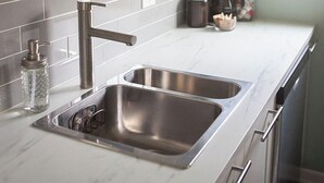 Une cuisine moderne dotée d’un évier en acier inoxydable, d’un plan de travail en marbre blanc et de murs vert clair.