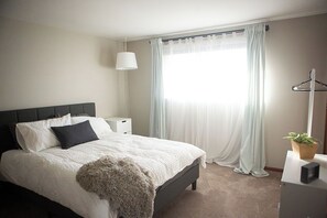 A bedroom with a bed, bedside tables, a lamp, a plant, and a window with curtains. - Bright, Modern Townhome with Natural Light (Westerville)