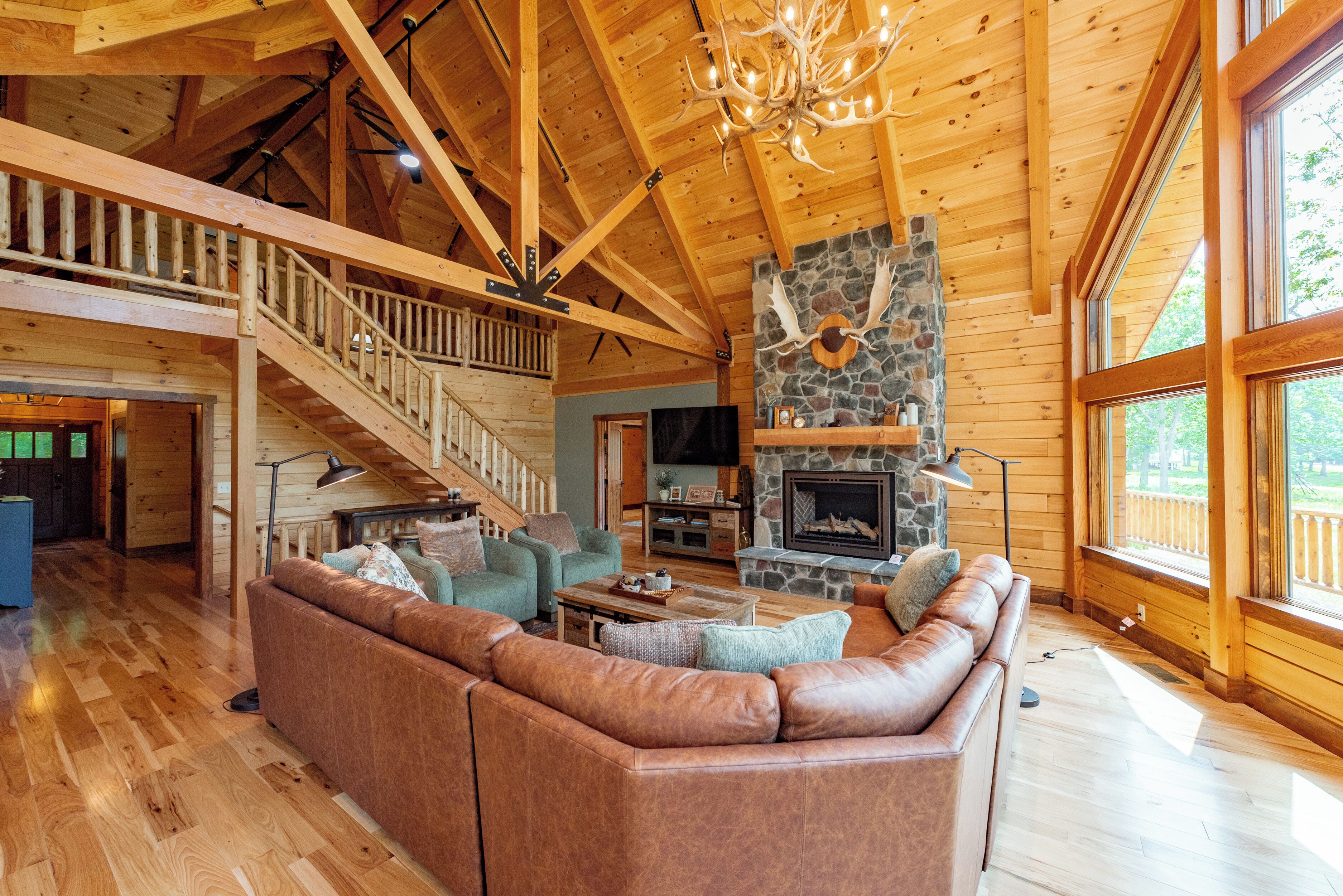 Ein geräumiger Holzraum mit Kamin aus Stein, einem Ledersofa und einer Treppe zu einer oberen Ebene.