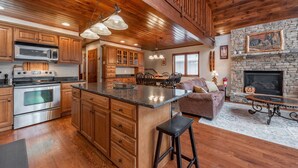A spacious kitchen with wooden cabinets, a large island, and a stone fireplace. - Cozy Lake Escape Near State Park & Slopes (Swanton)