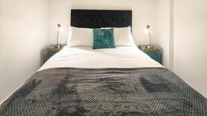 A bedroom with a large bed, a headboard, two bedside tables, a wall-mounted lamp, and a framed picture above the bed. - The County Staycation (Liverpool)