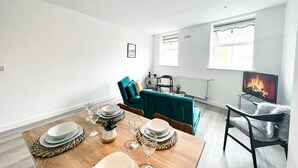A modern living room with a dining table set for six, a teal sofa, and a TV displaying a fire. - The County Staycation (Liverpool)
