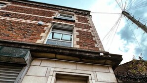 A building with a black entrance door, a metal vent, and a brick facade. - The County Staycation (Liverpool)