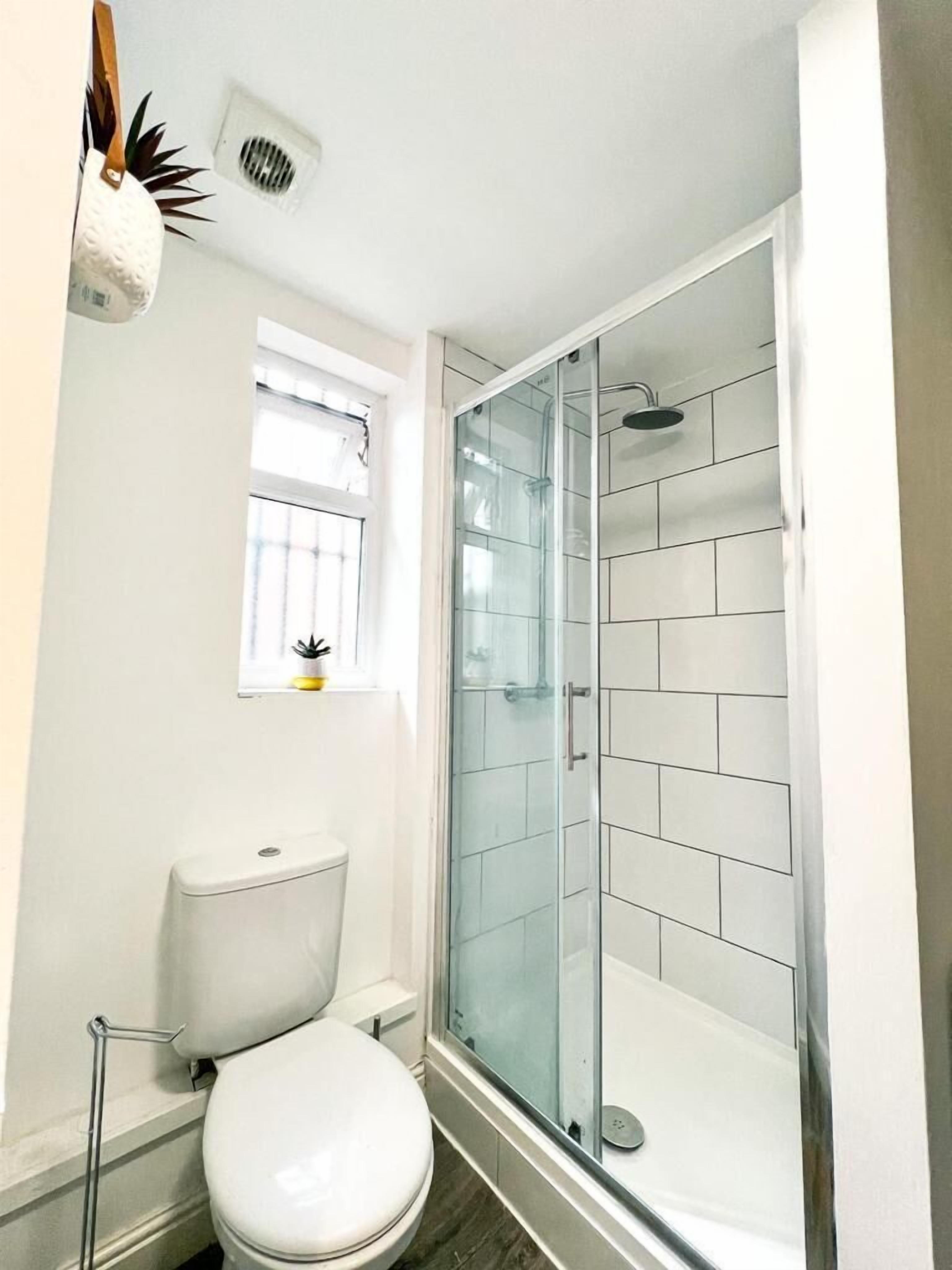 A bathroom with a toilet, a glass shower enclosure, and a window with blinds.